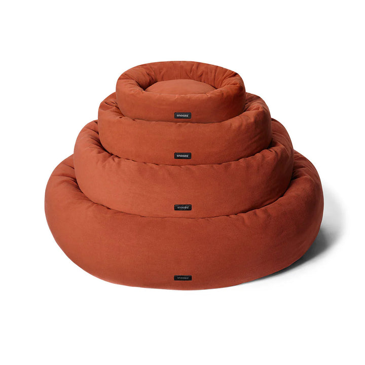 Various sizes of the Snooza Self-Warming Polar Fleece Cuddler in Rust stacked on top of each other on a white background.